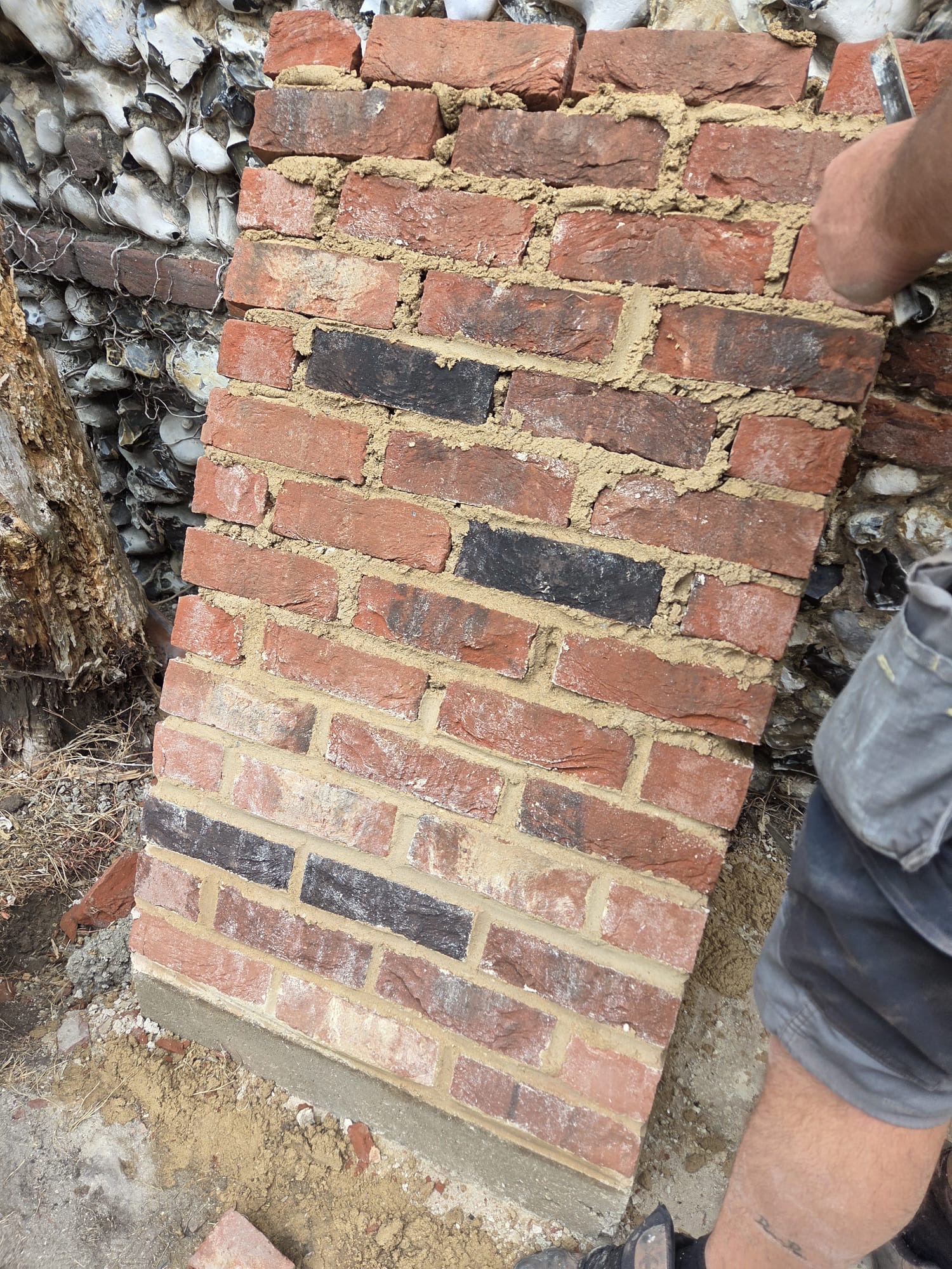 Handmade brick pier being built into a Norfolk flint wall